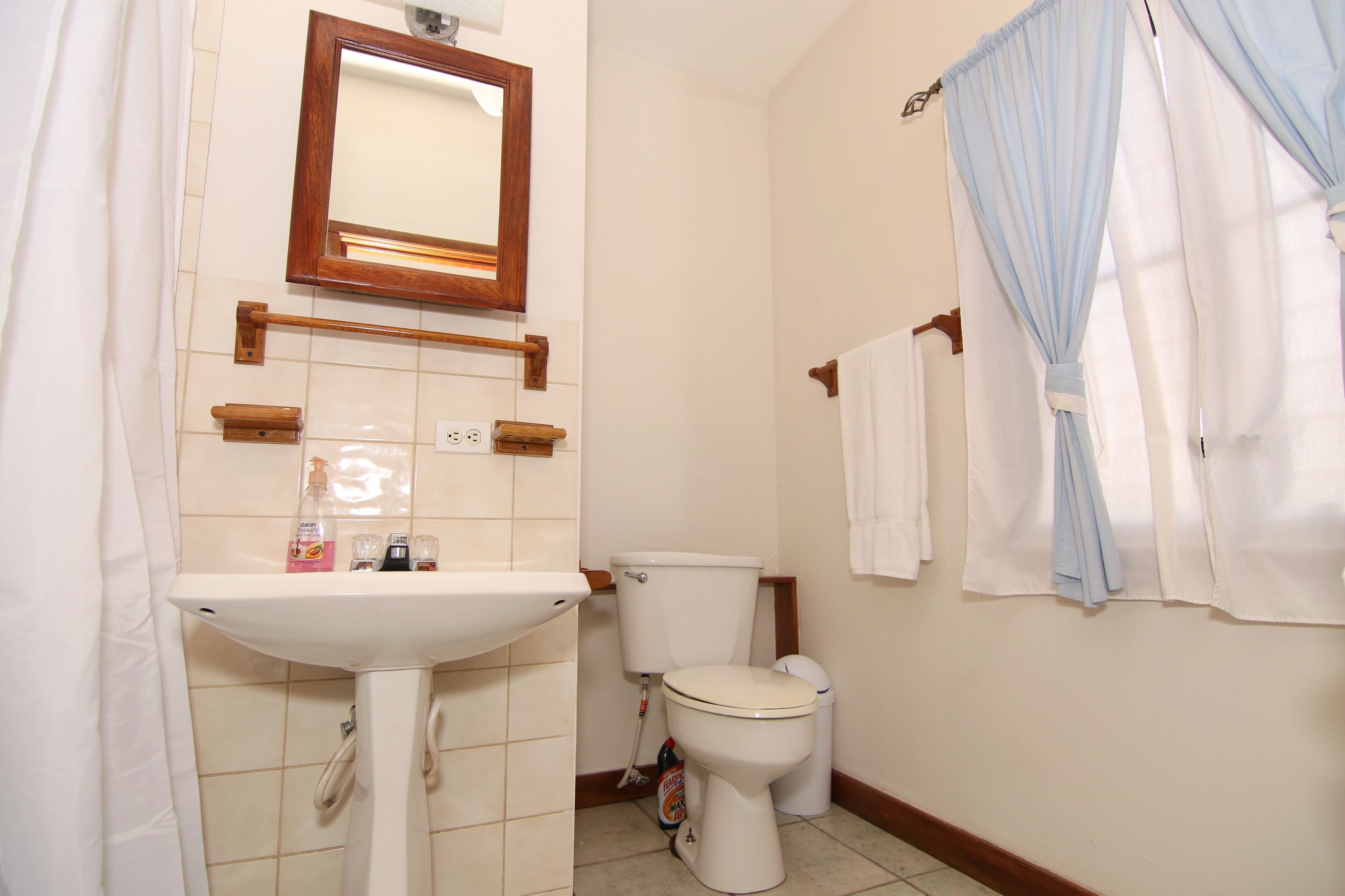 Ein Badezimmer mit einem weißen Waschbecken, Spiegel und Toilette. Handtücher hängen an der Wand und ein Duschvorhang ist angebracht.