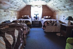 Ein kleines, gemütliches Schlafzimmer im Dachgeschoss mit zwei Betten, einem Nachttisch und einer Lampe.