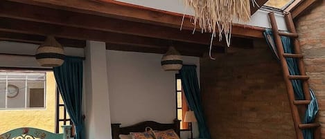 A bedroom with two beds, wooden beams, a slanted ceiling, and a ladder against the wall.