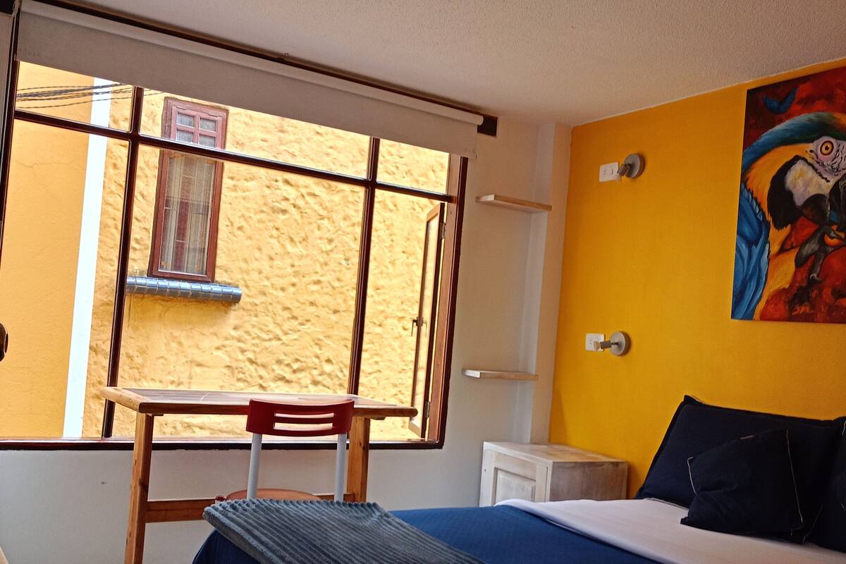 Une chambre à coucher avec un lit, un bureau, une chaise, une fenêtre et un tableau au mur.
