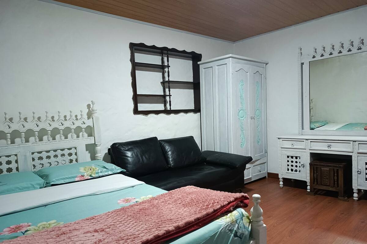 Une chambre à coucher comprenant un lit, un canapé en cuir noir, une armoire blanche et une commode.