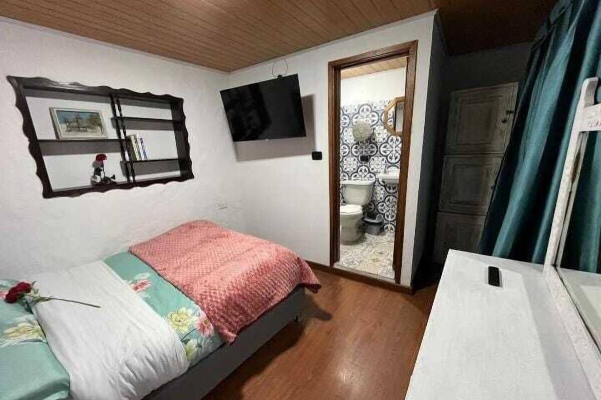 Une chambre à coucher avec un lit, une télévision, une armoire et une salle de bain visible à travers une porte ouverte.