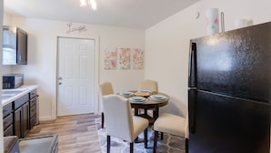 A compact kitchen with a black refrigerator, a microwave, and a dining table set for four.