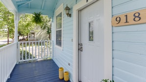 A porch with a white door, a wooden number sign, and a hanging plant.