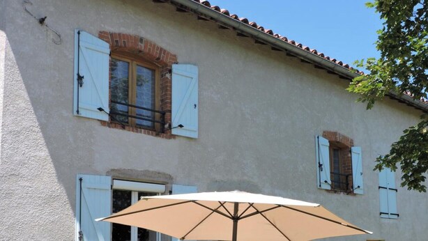 A rustic building with a patio area featuring a table and chairs, an umbrella, and potted plants. - Cottage Les Hortensias in Pralong - Charm and Comfort for 4 Guests with Internet (Pralong)