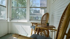 A corner room with a large window, wicker furniture, and a small table with a plant.