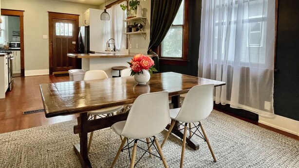 A dining area with a wooden table, white chairs, a chandelier, and a vase with flowers.