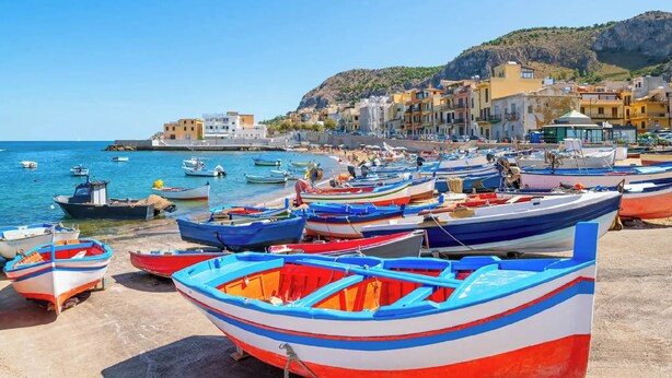 A coastal town with colorful boats docked along the shore, buildings in the background, and a clear sky. - Ludovica's dream house  (Bagheria)