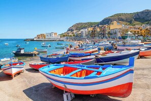 A coastal town with colorful boats docked along the shore, buildings in the background, and a clear sky. - Ludovica's dream house  (Bagheria)