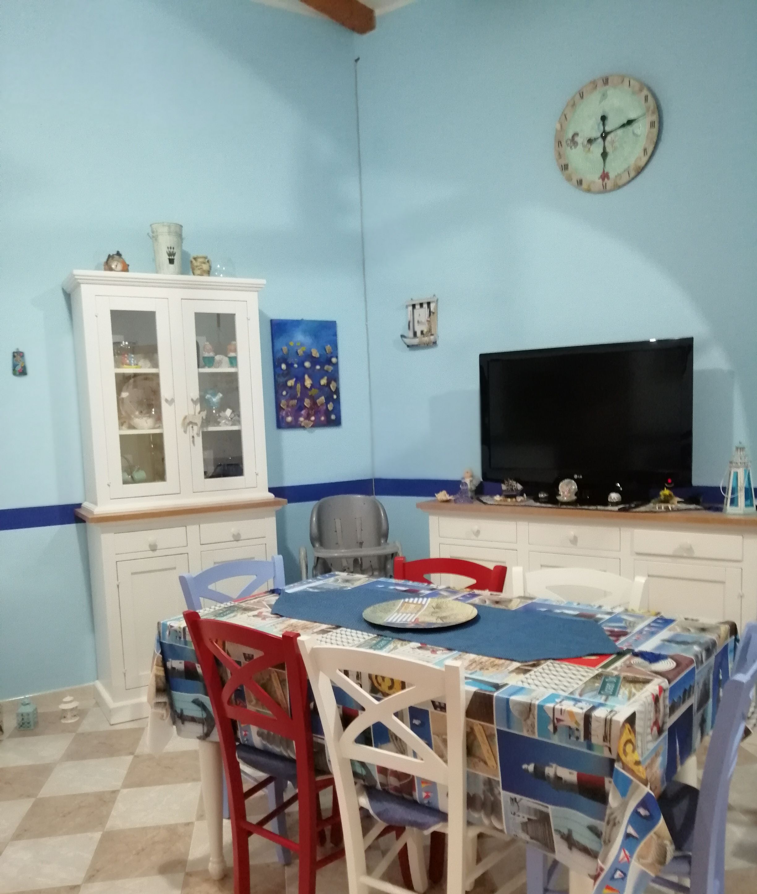 Un comedor con una mesa preparada para dos, un televisor y un aparador con puertas de vidrio.