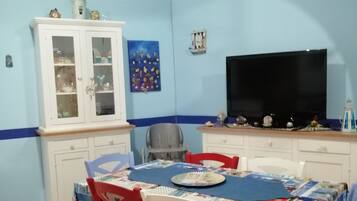 Un comedor con una mesa preparada para dos, un televisor y un aparador con puertas de vidrio.