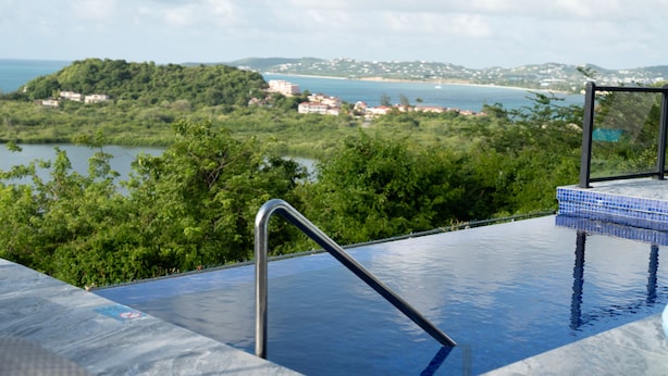 A swimming pool with a view of a coastal landscape, including a beach and hills.