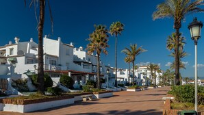 Un paseo marítimo con edificios blancos, palmeras y un cielo azul despejado.