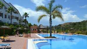 Una piscina con sillas de descanso, palmeras y un edificio con balcones.