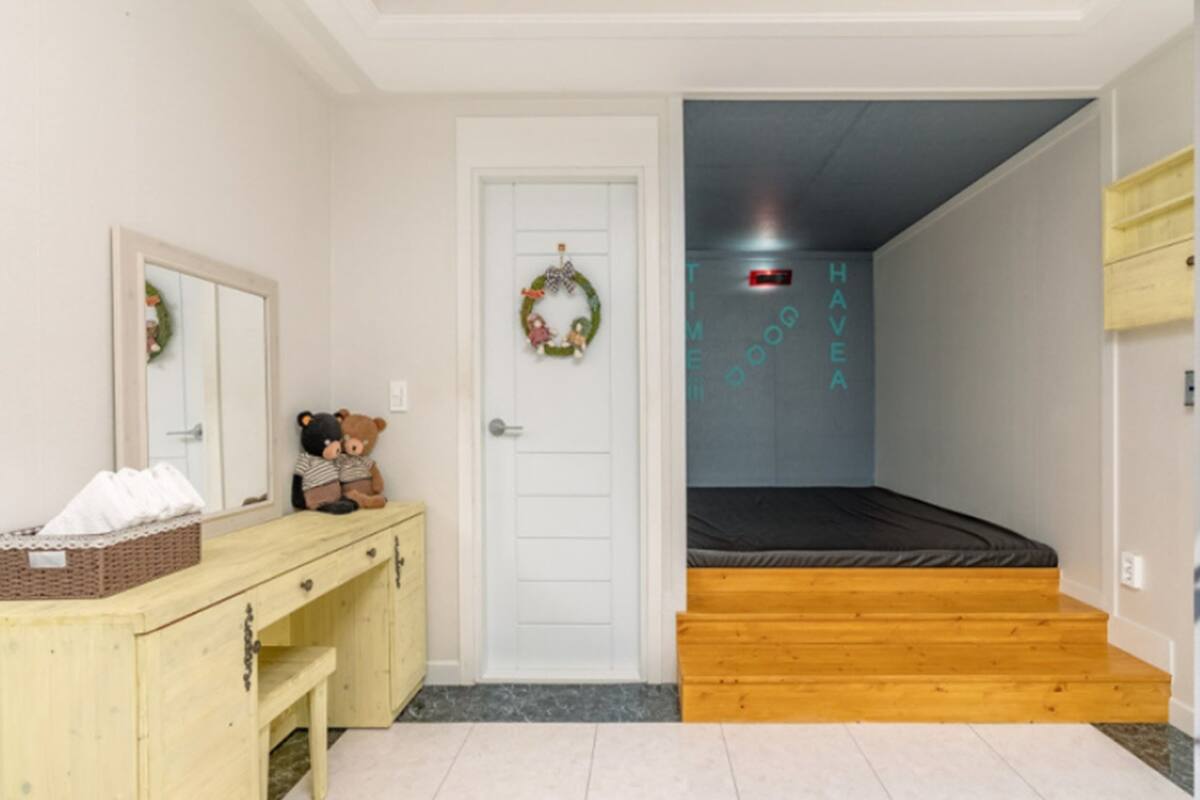 A bedroom with a wooden bed, a dresser, a mirror, and a door with a wreath.