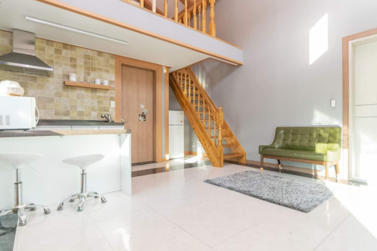 A modern kitchen with a wooden staircase, a green sofa, and a white door.