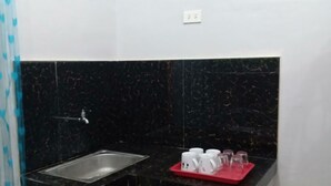 Uma pequena cozinha compacta com reboco de mármore preto, uma pia e um tabuleiro vermelho com chávenas.