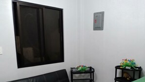 Quarto com sofá de couro preto, janela, prateleira pequena preta com um cacto e bancada verde.