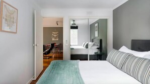 A modern bedroom with a large bed, a desk, and a chair in the adjacent room. - Southbank Boulevard Melbourne (Southbank)