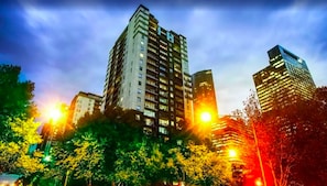 A high-rise building with multiple floors and balconies, surrounded by trees and streetlights.