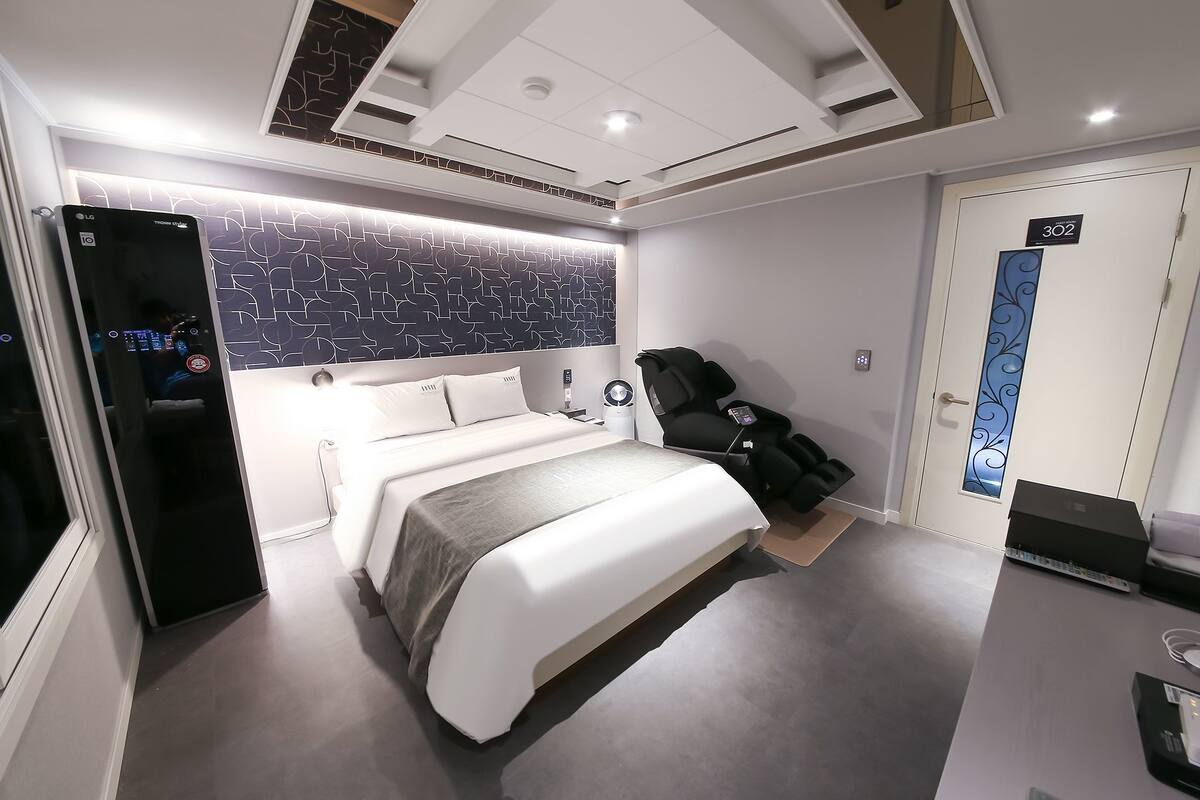 Quarto de hotel moderno com uma cama grande, poltrona de massagem e minibar.