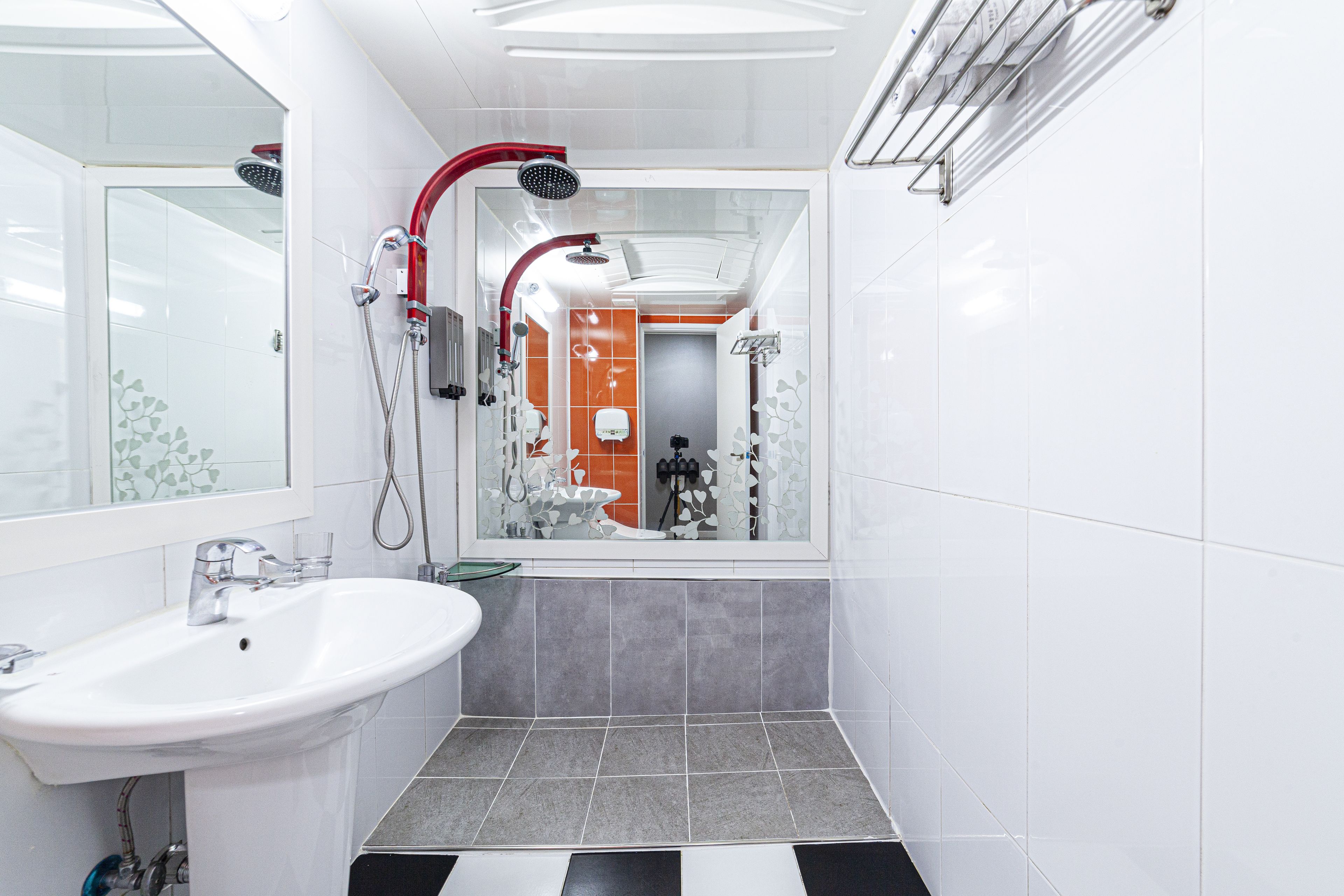 Un baño con lavamanos blanco, ducha con manguera roja y suelo de baldosas grises.