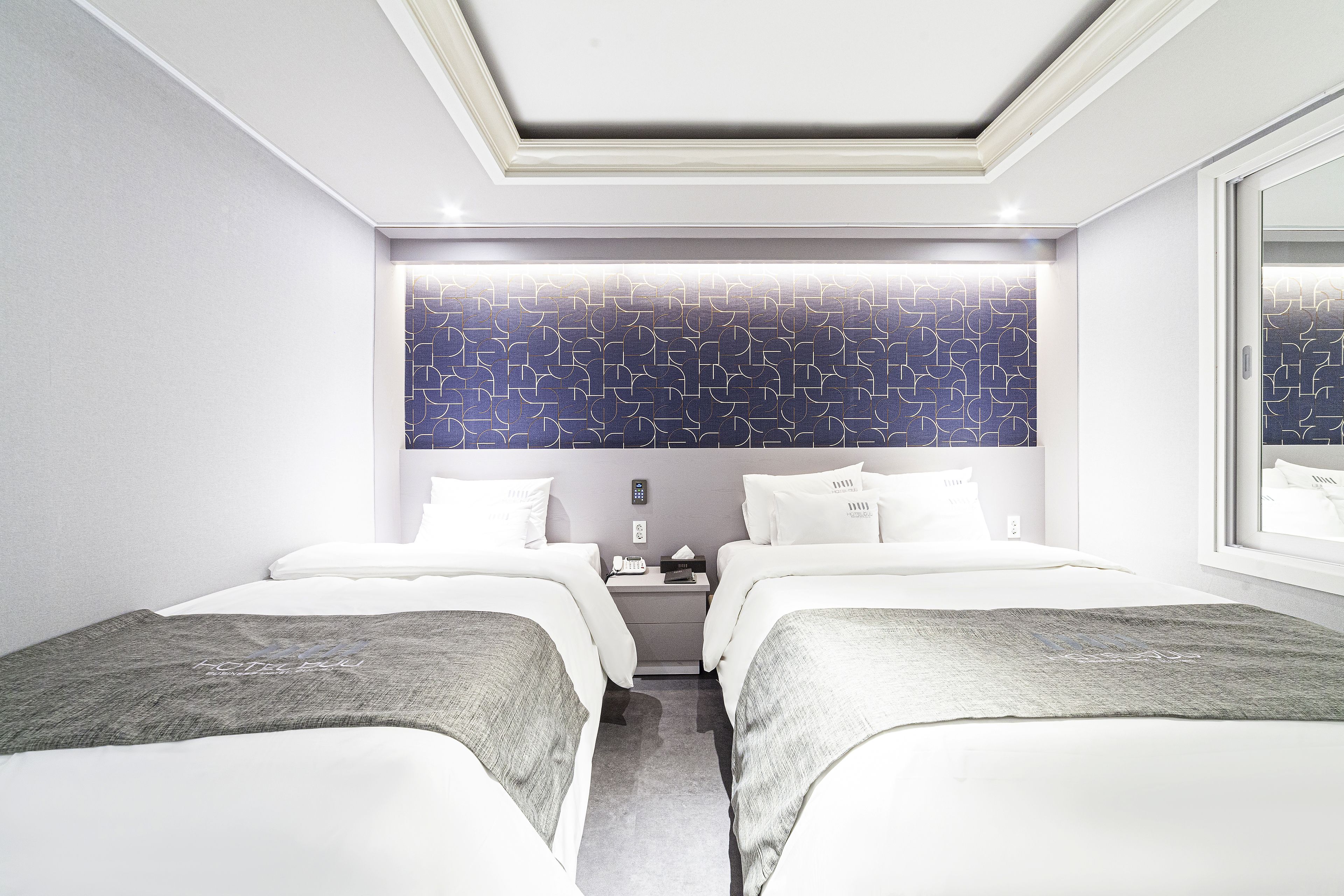 Una habitación de hotel moderna con dos camas, una mesita de noche y un espejo grande.