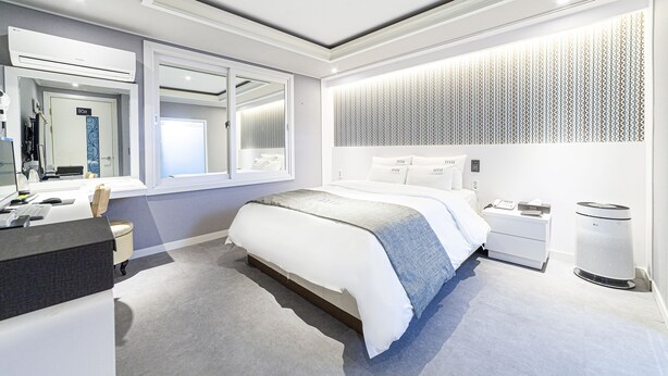 A modern bedroom with a large bed, bedside tables, a desk, and a mirror. - Business Hotel Duu (Gwangju)