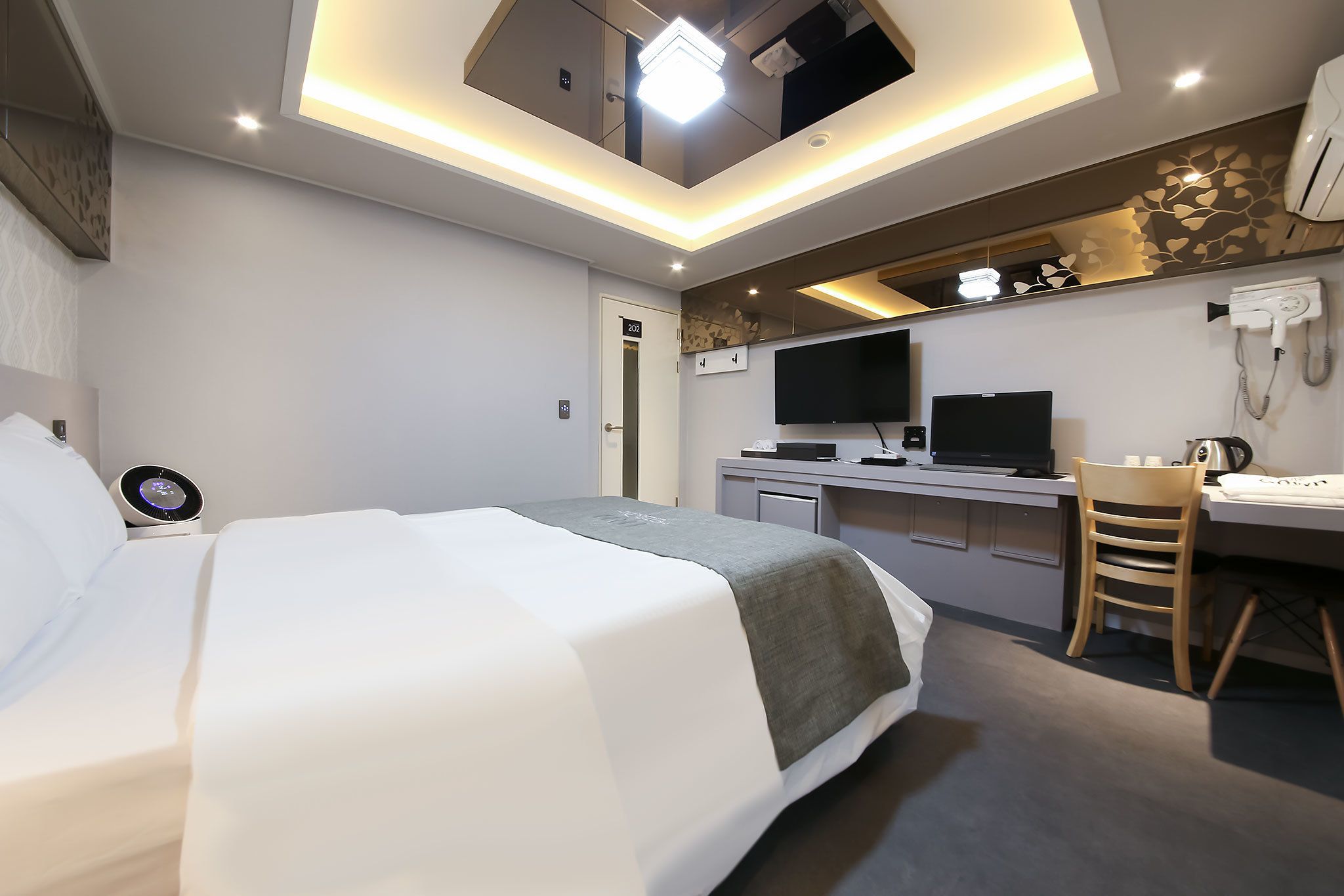 A modern hotel room with a large bed, a desk, a chair, a flat-screen TV, and a hairdryer.