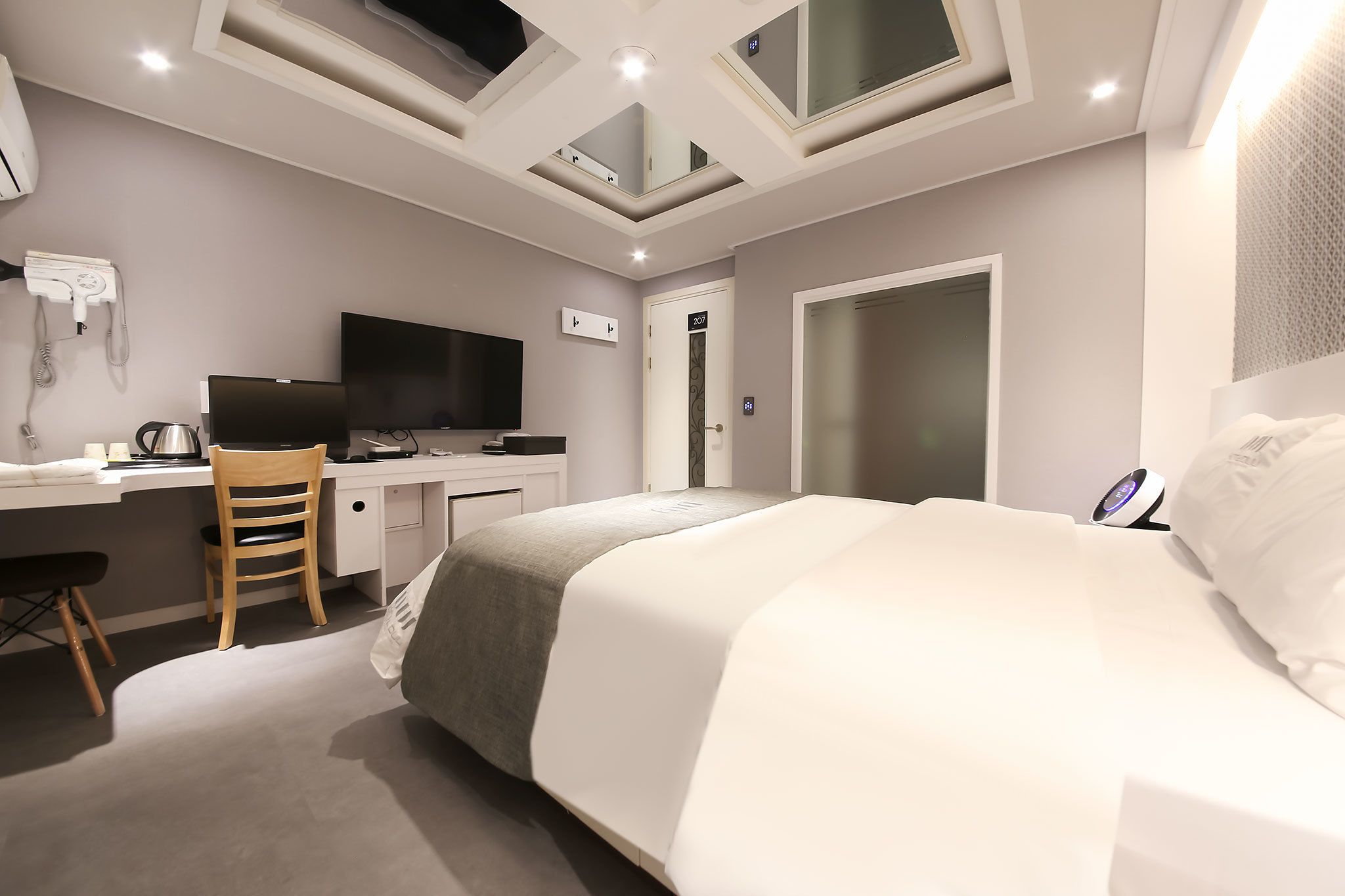 Et moderne hotelværelse med seng, skrivebord, stol og et fladskærms-TV.