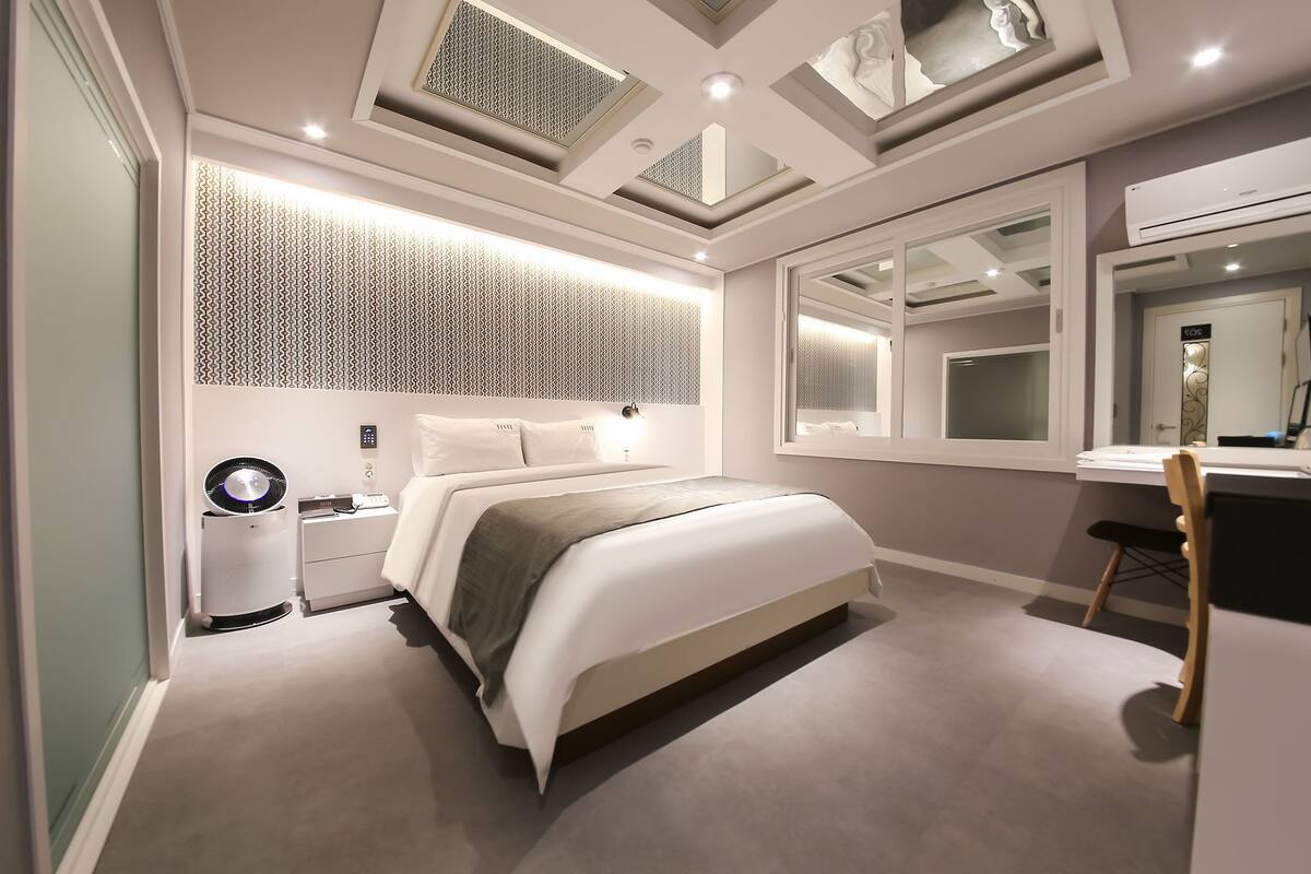 Quarto moderno com cama, mesa de cabeceira e espelho.