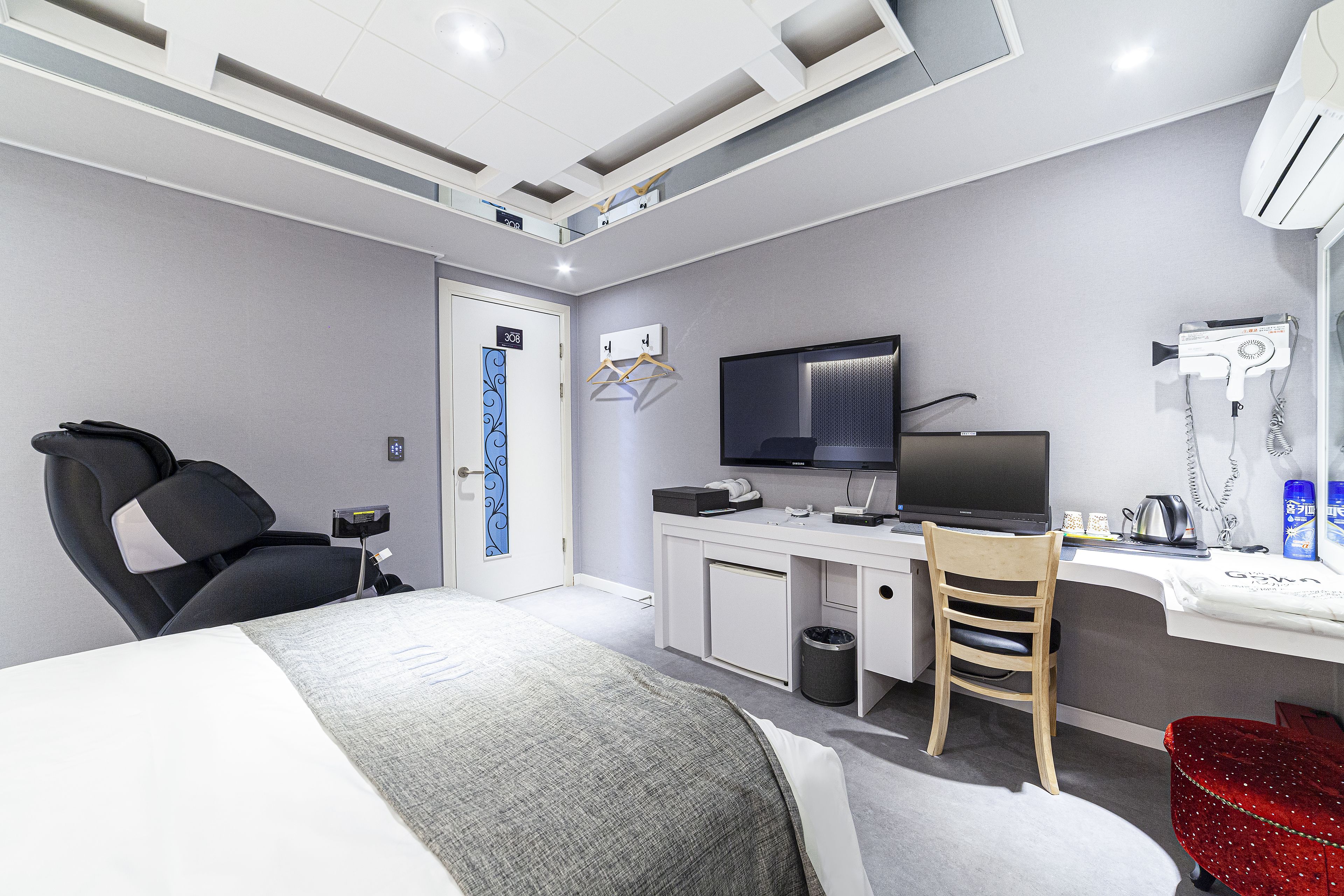 Een moderne hotelkamer met een bed, een bureau, een stoel, een televisie en een haardroger.
