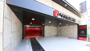 A hotel entrance with a modern European style sign, a red interior visible through the doorway, and a sign indicating a parking lot. - Business Hotel Duu (Gwangju)