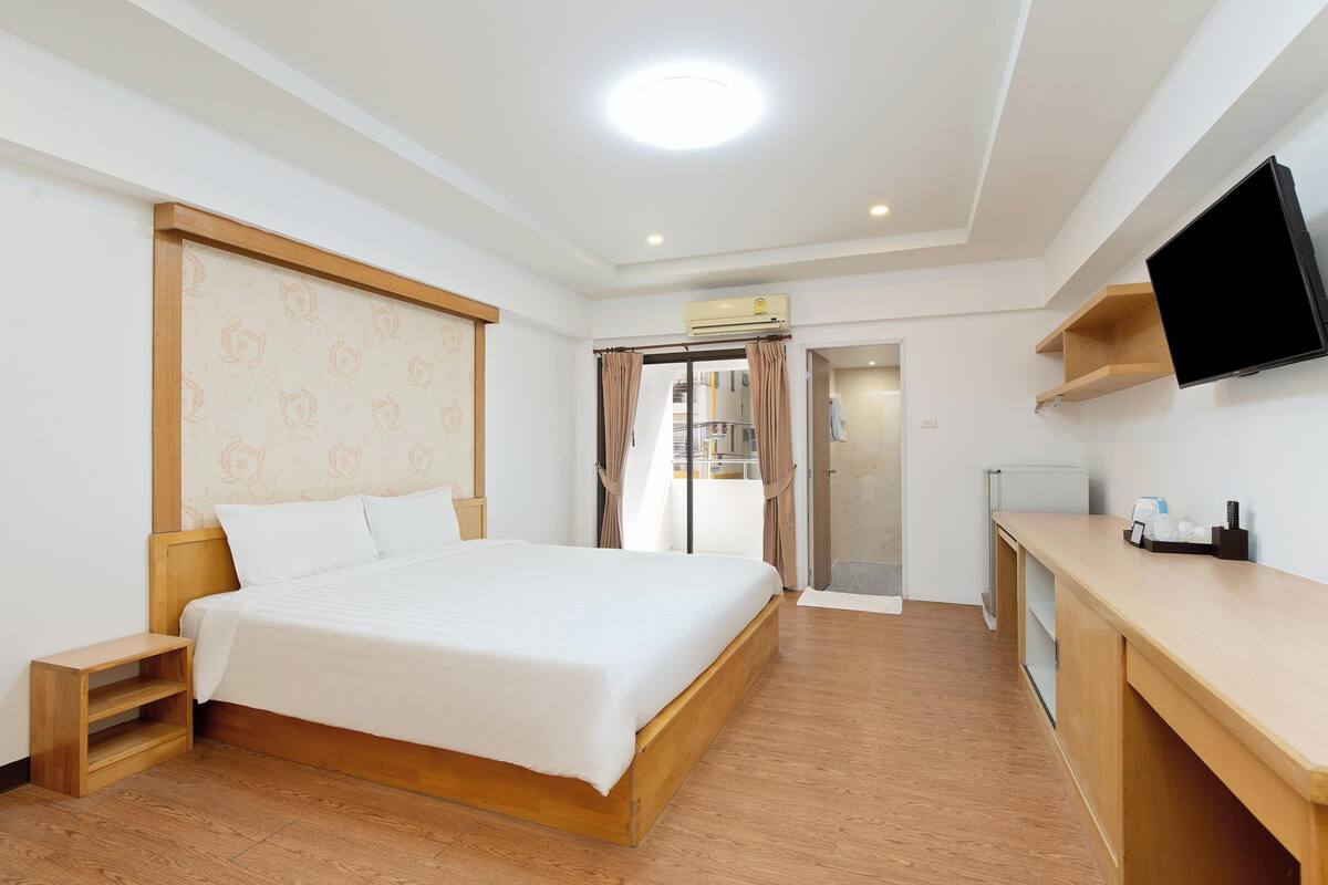 Ein modernes Hotelzimmer mit einem hölzernen Bett, einem Flachbildfernseher, einem Schreibtisch und einem Balkon mit Glastür.