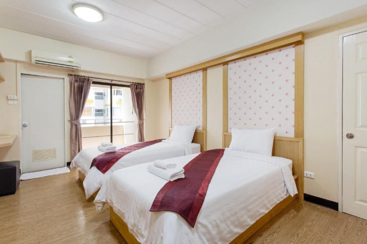 Une chambre d’hôtel avec deux lits, une fenêtre avec des rideaux, un appareil de climatisation et une porte.