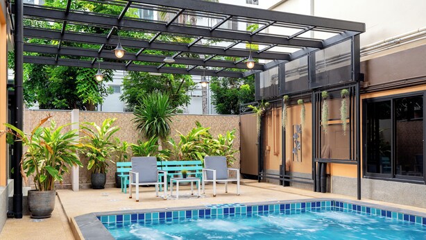 Piscina com borda azulejada, cercada por plantas em vasos e mobiliário de exterior.