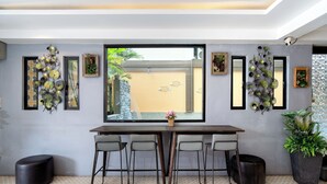 Uma sala de jantar moderna com uma janela grande, uma mesa com quatro cadeiras, obras de arte decorativas e plantas em vasos.