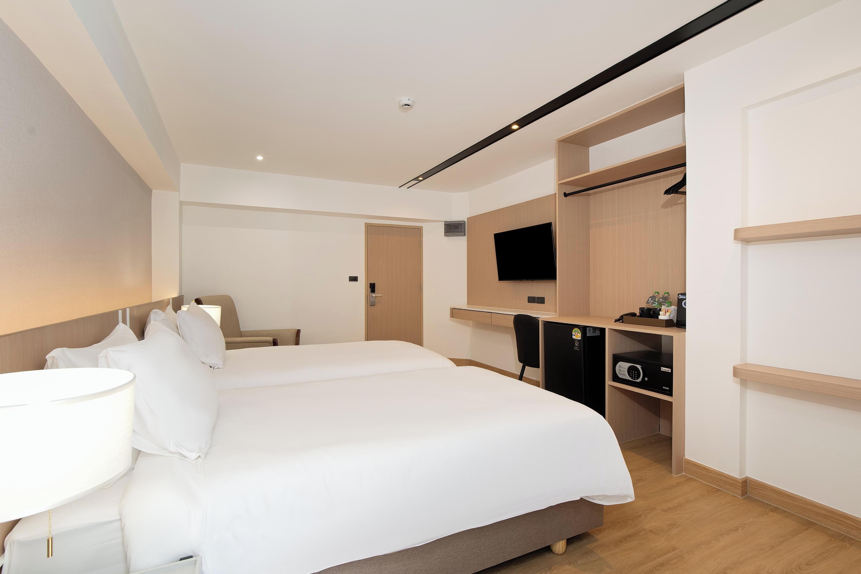 A hotel room with a large bed, a desk, a chair, a TV, and a wardrobe.