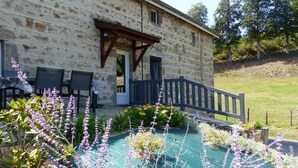 Ein Steinhaus mit überdachter Terrasse, Außenbestuhlung und einem Garten mit violetten Blumen.