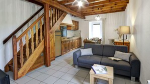 Ein großzügiger Wohnbereich mit einer Holztreppe, einem grauen Sofa, einem kleinen Tisch und einer Küche im Hintergrund.