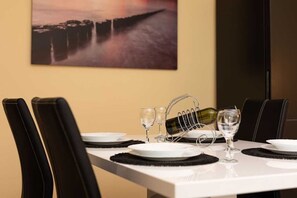 A dining table set with plates, glasses, and a wine bottle holder, with chairs and a painting on the wall.