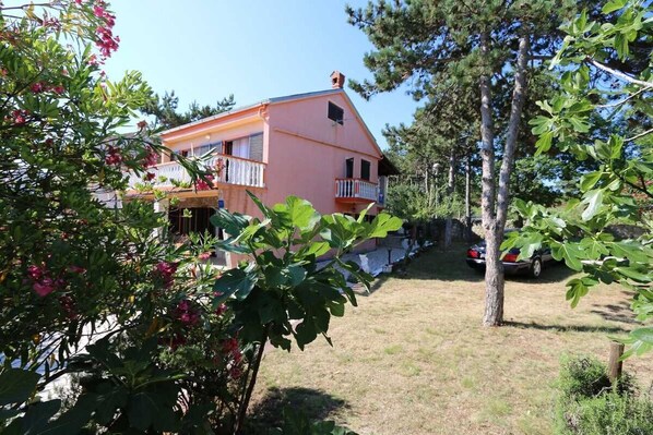A two-story house with a balcony, surrounded by trees and a car parked in the driveway. - Apartment Vugrin Oleander A4 (Silo - island Krk)