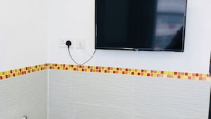 A bathroom with a tiled wall, a flat-screen TV mounted above a tiled baseboard, and a power outlet.