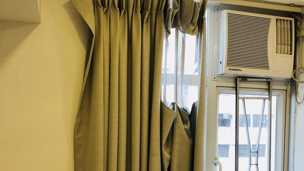 A room with a window, a curtain, and an air conditioning unit mounted on the wall.