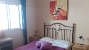 Een slaapkamer met een bed, nachtkastjes, een lamp en een schilderij aan de muur.