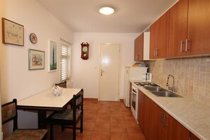 A compact kitchen with wooden cabinets, a tiled backsplash, a sink, and a dining area with a table and chairs.