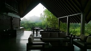 An outdoor seating area with tables and chairs, a sofa, and a view of a lush green landscape. - Go Go Green Resort (Habarana)