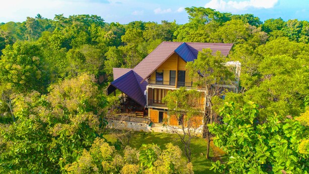 A two-story house surrounded by dense greenery, with a sloped roof and a balcony on the upper floor. - Go Go Green Resort (Habarana)