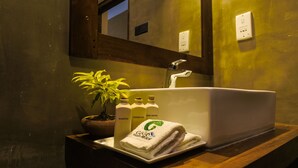 A bathroom with a white sink, a potted plant, and three bottles of toiletries. - Go Go Green Resort (Habarana)