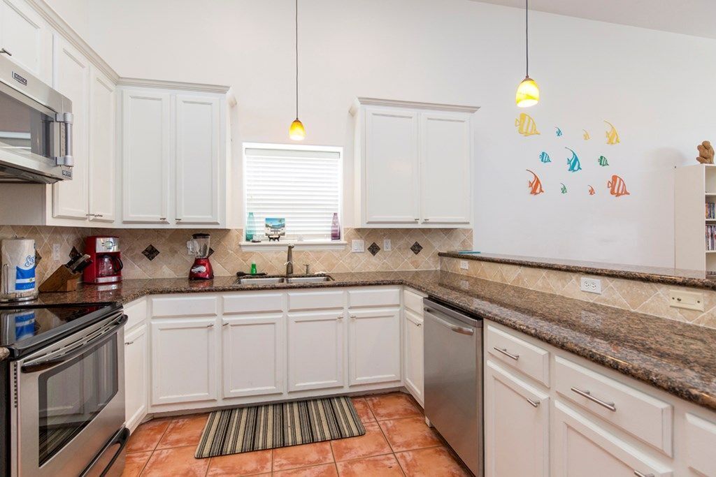 A kitchen with white cabinets, a granite countertop, a stove, and a dishwasher.